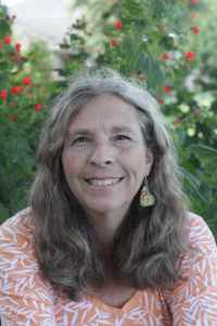 Carol Clark smiles with red flowers in the background.