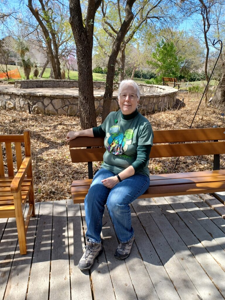 Smiling Volunteer Judy Rowe sitting on a bench under a tree at the Heard Museum.