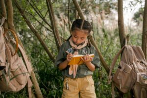 A young girl scout takes notes during a summer camp in the woods.
