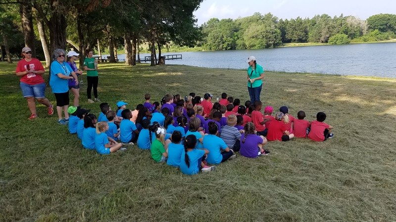 Photo of students listening to educational presentation beside lake