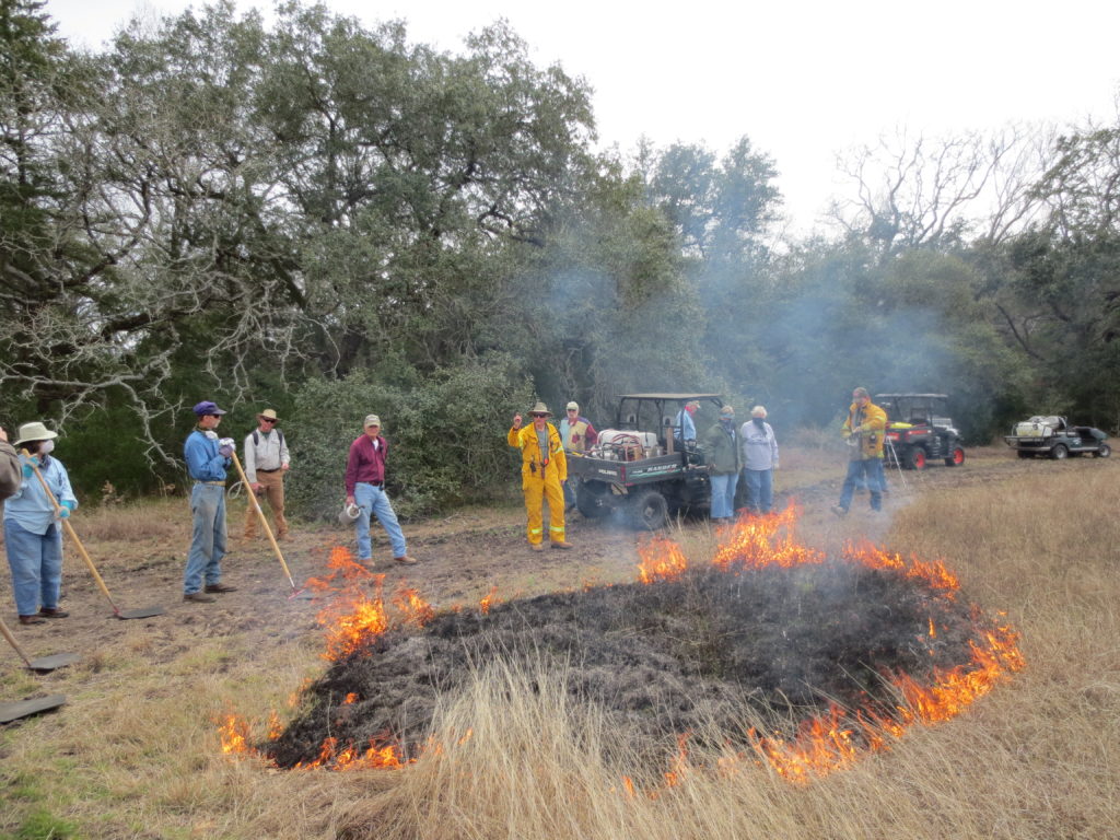 Participants gathered around burn area wearing protective clothing.