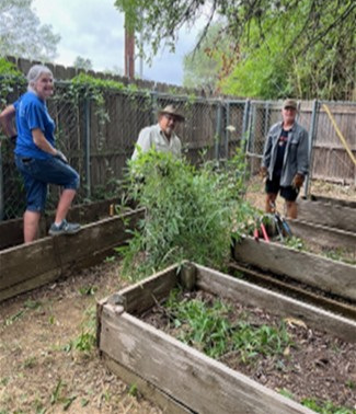 3 people working on planting beds in a fenced area.