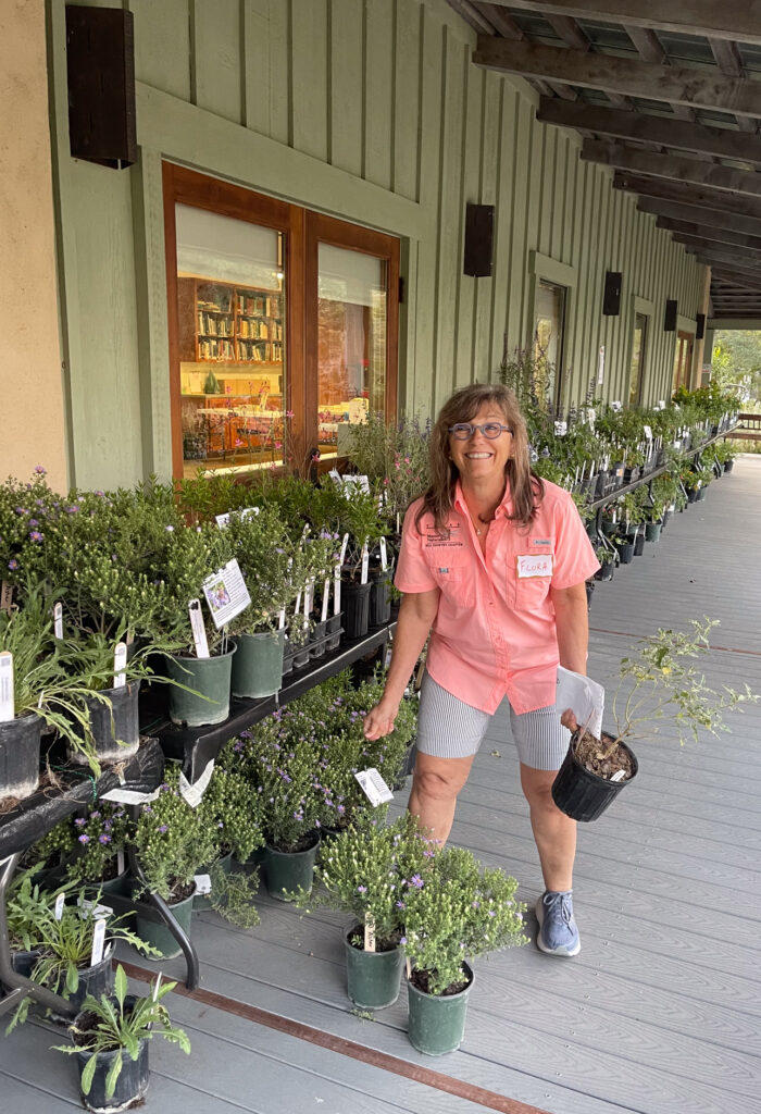 woman in front of tables and potted plants picking up potted plants