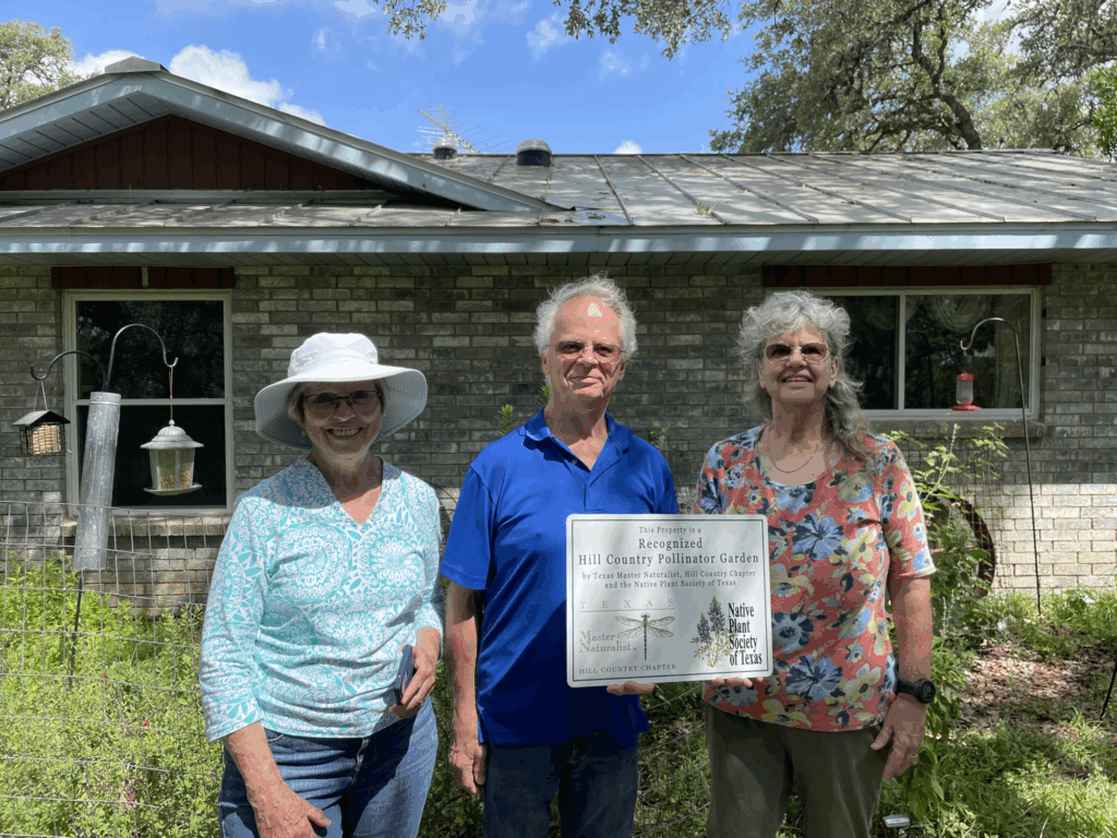 3 people in a garden displaying a Pollinator Garden Recognition sign