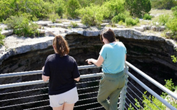 two people looking over railings into the great maw at the Devil's Sinkhole SNA, Texas