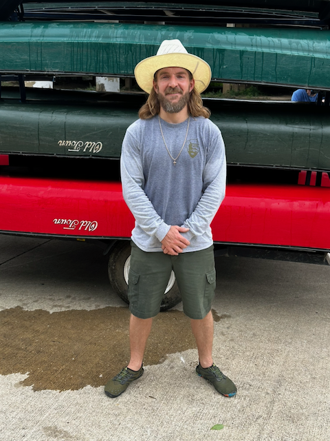 National Park Service Ranger Max Harper standing in front of stacked canoes.