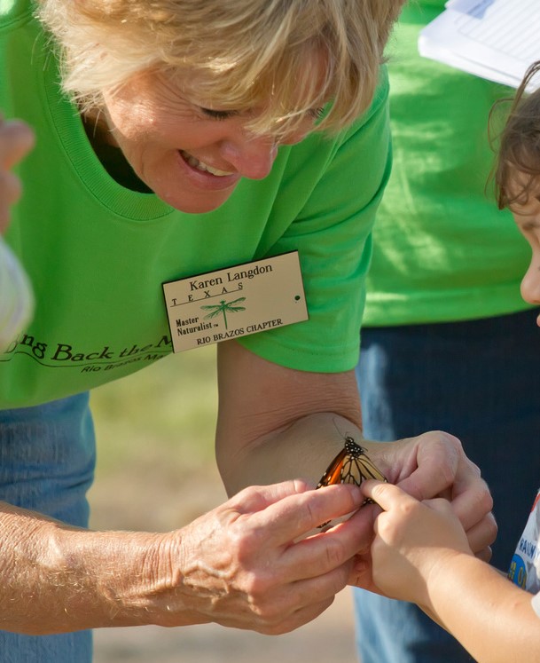 A Master Naturalist (woman) showing a child how to tag a Monarch butterfly.